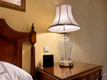 Photo of Lamp and electric clock on wooden bedside in luxury hotel