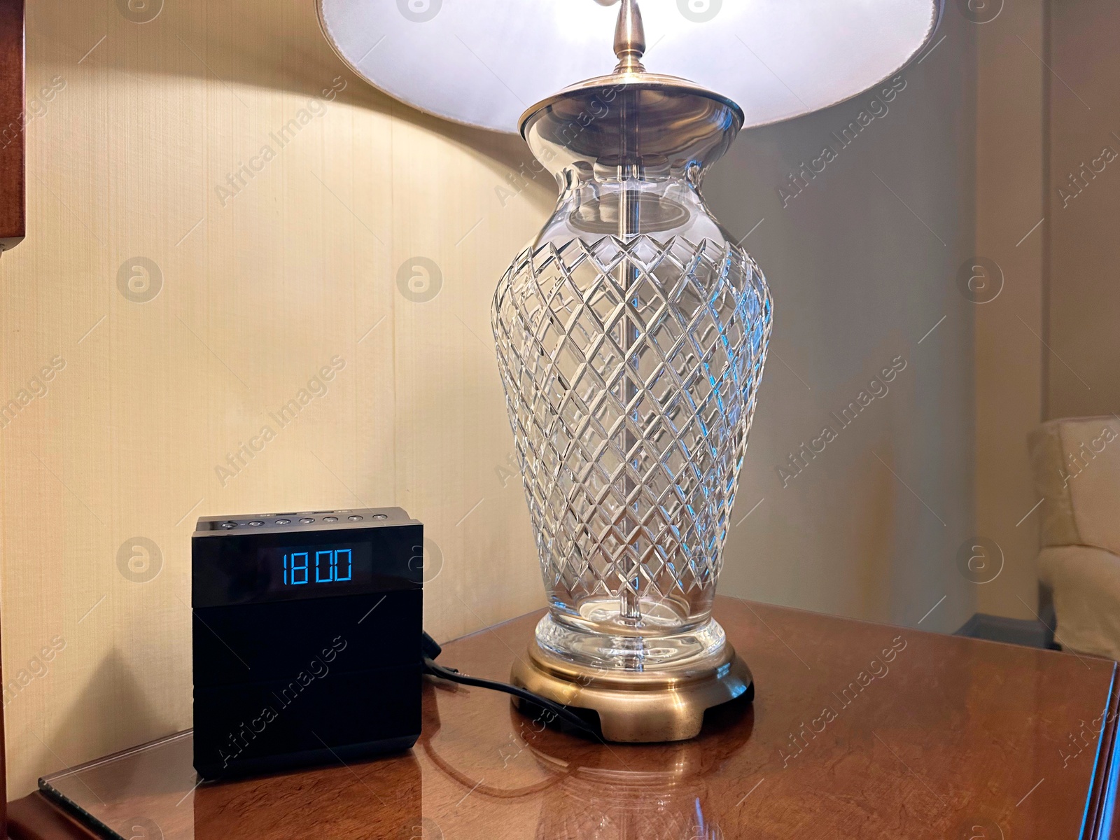 Photo of Lamp and electric clock on wooden bedside in luxury hotel