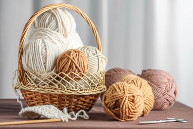 Photo of Skeins of soft yarn, knitting needles and scissors on brown fabric indoors