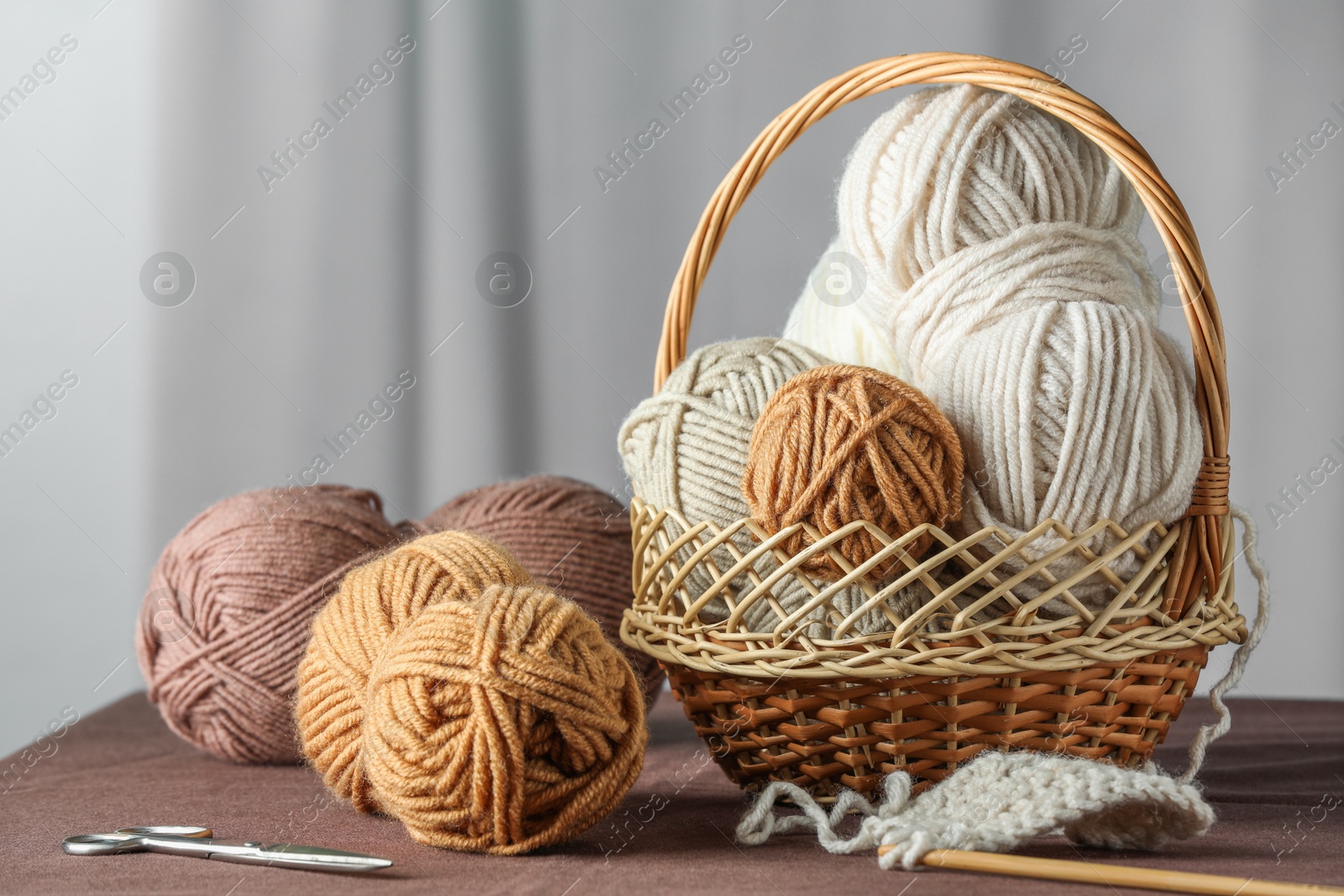 Photo of Skeins of soft yarn, knitting needles and scissors on brown fabric indoors