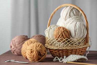 Photo of Skeins of soft yarn, knitting needles and scissors on brown fabric indoors