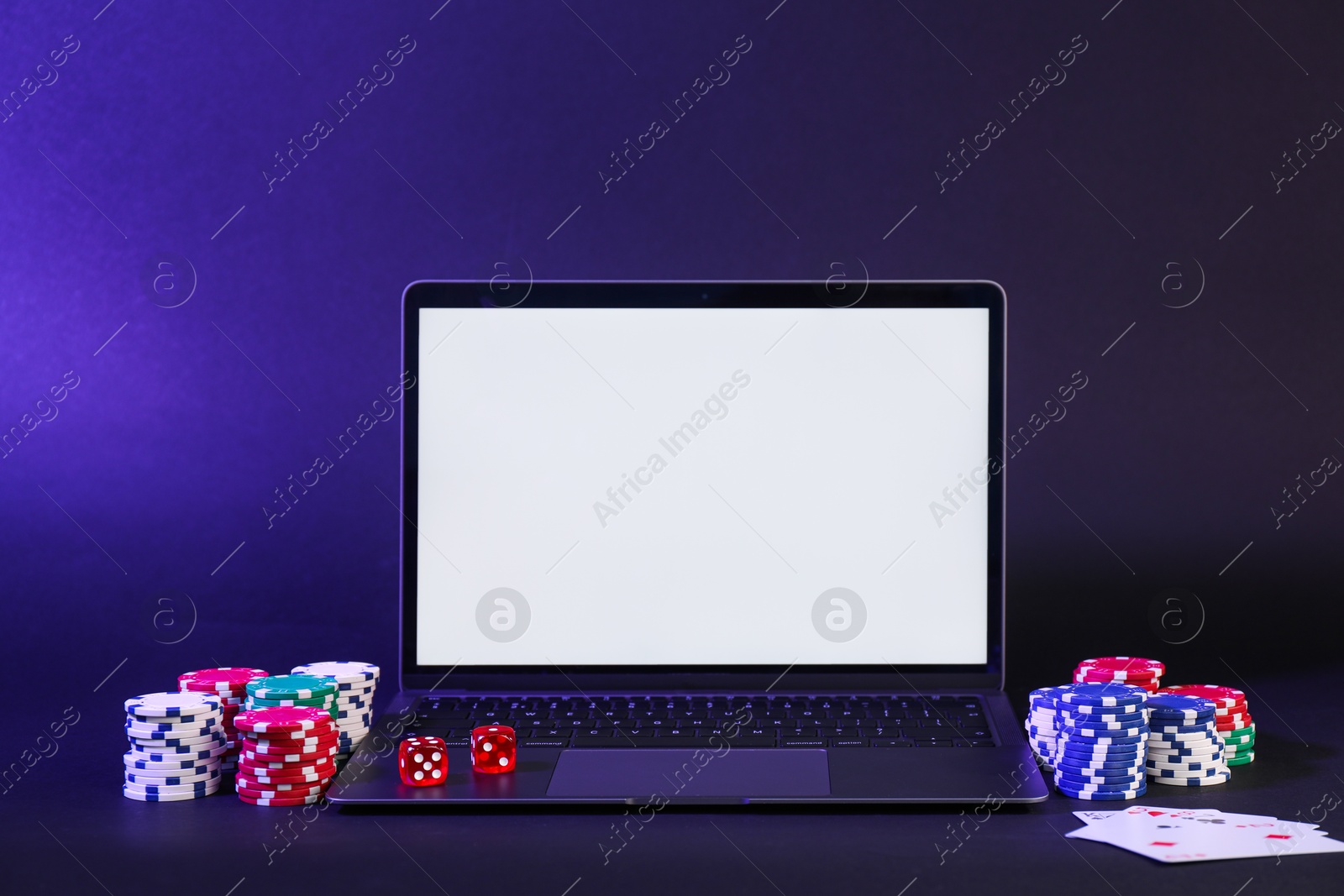 Photo of Online poker. Playing cards, chips, dice and laptop on dark table