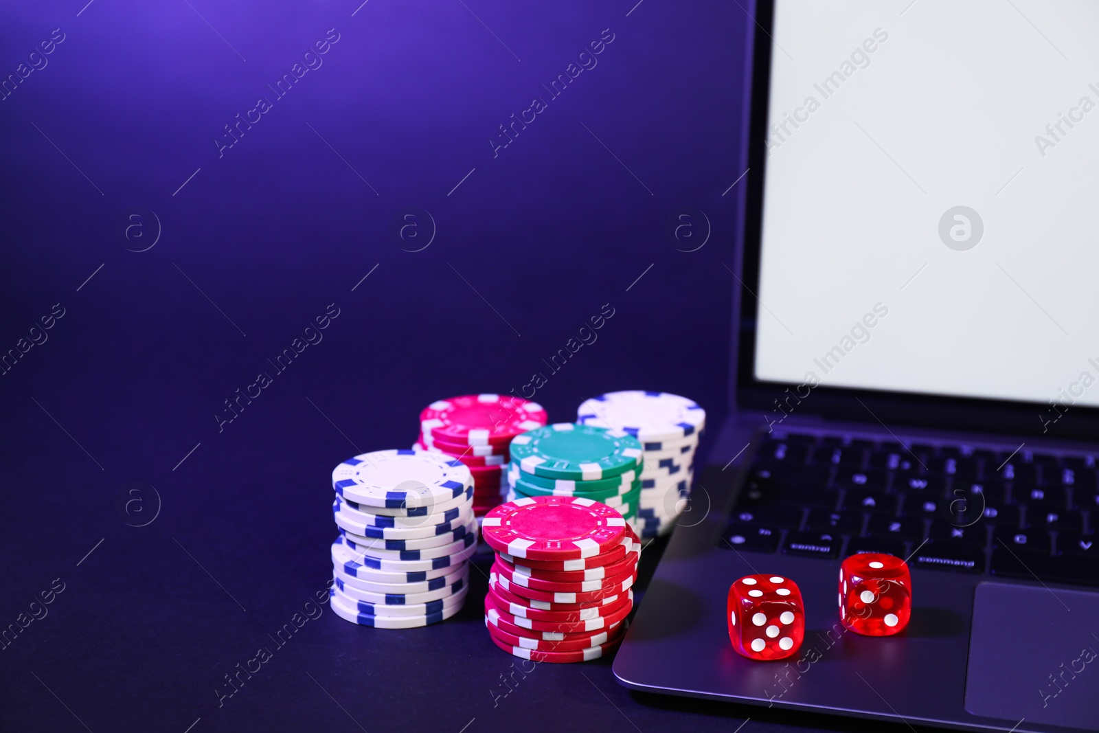 Photo of Online poker. Chips, dice and laptop on dark table, closeup