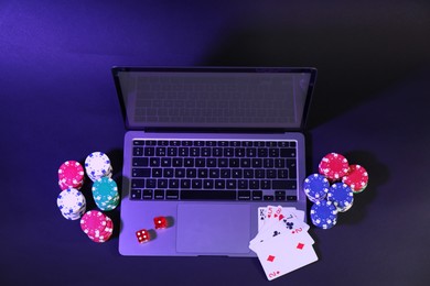 Photo of Online poker. Playing cards, chips, dice and laptop on dark table, above view