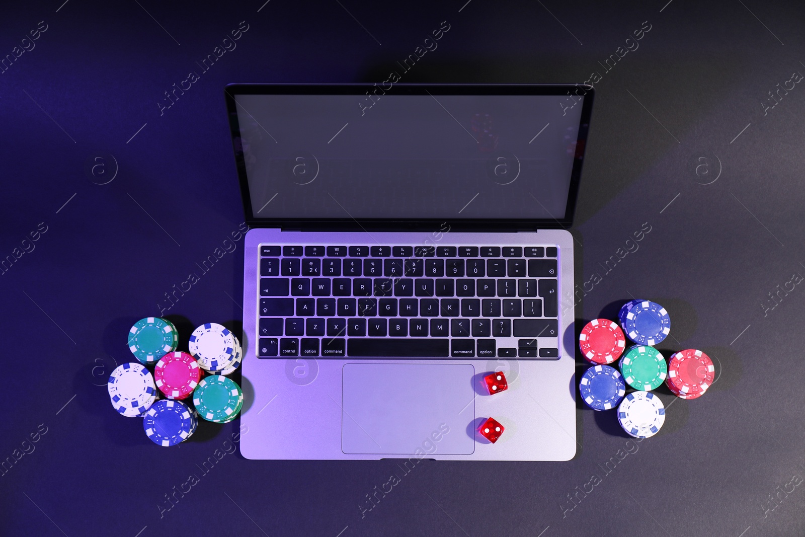 Photo of Online poker. Chips, dice and laptop on dark table, above view