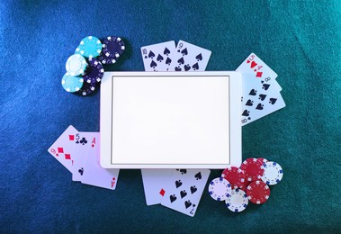 Photo of Online poker. Playing cards, chips and tablet on green table, top view