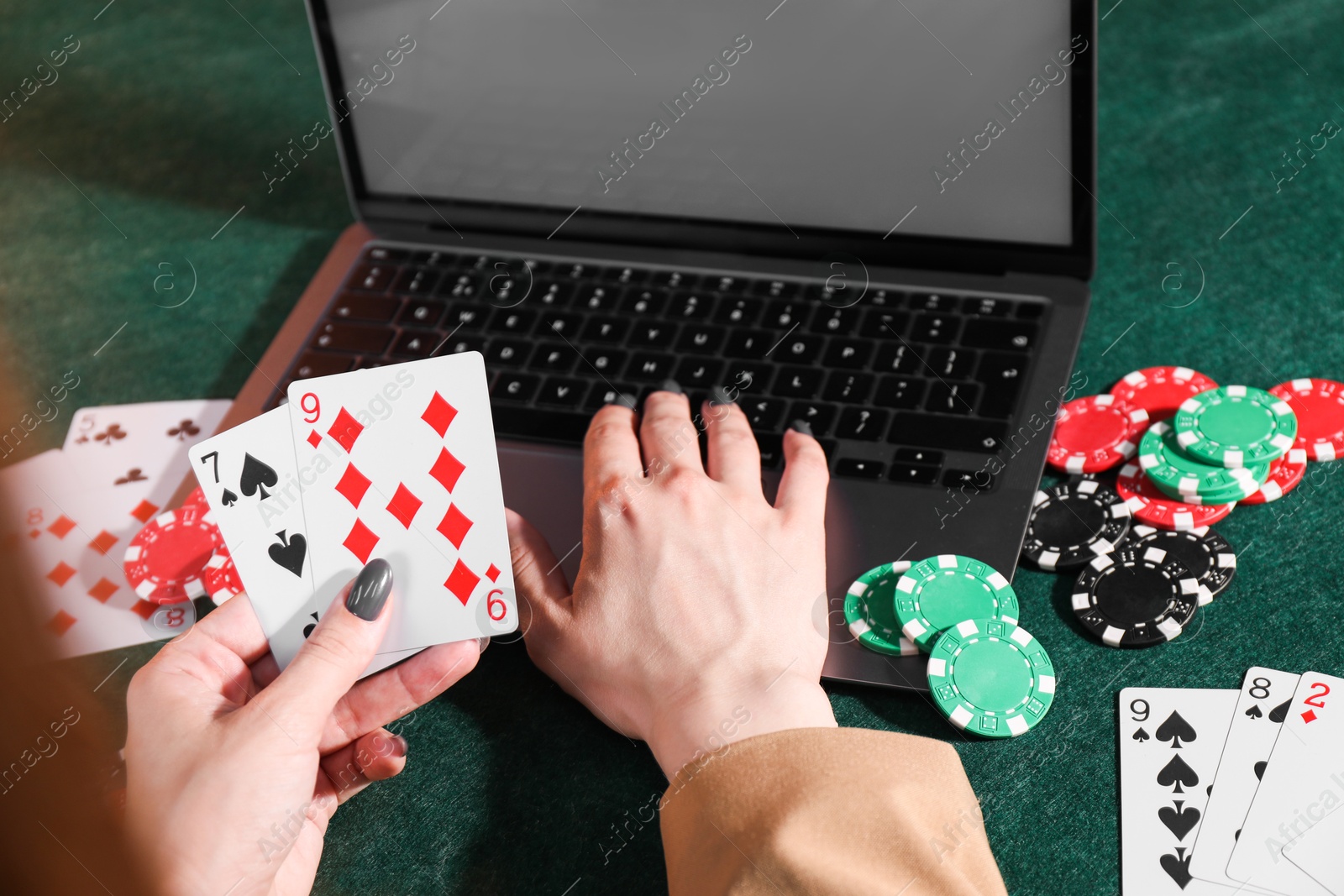 Photo of Online poker. Woman holding playing cards and using laptop at green table, closeup