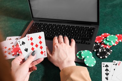 Online poker. Woman holding playing cards and using laptop at green table, closeup