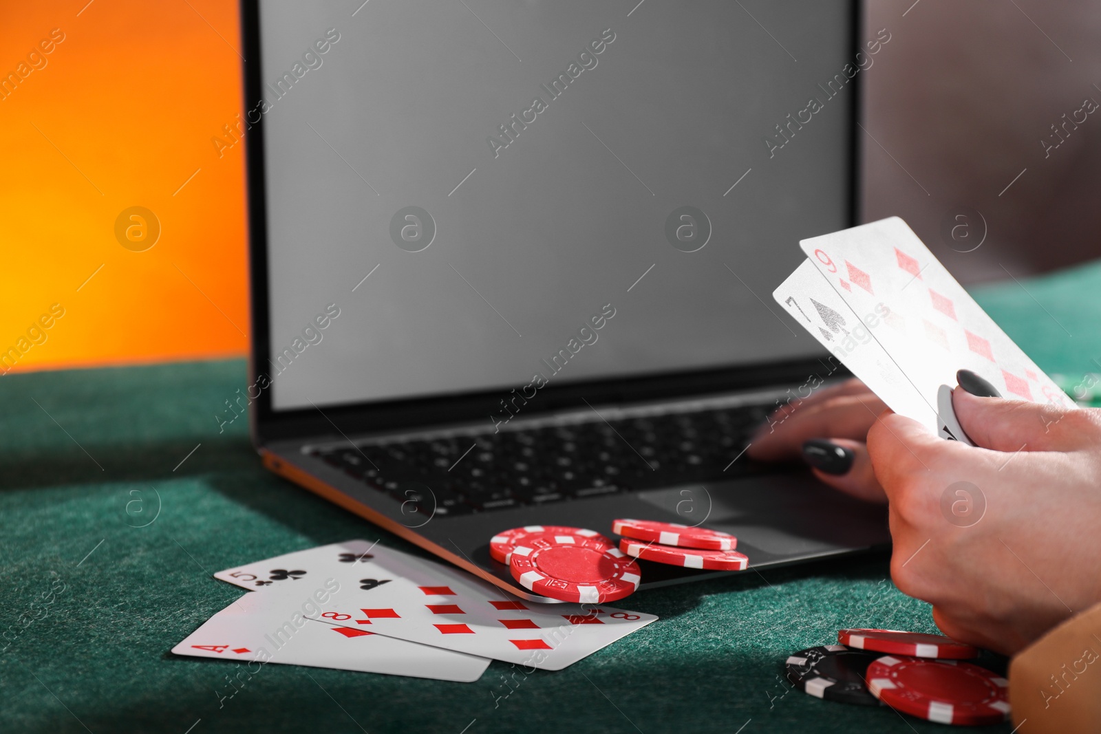 Photo of Online poker. Woman holding playing cards and using laptop at green table, closeup