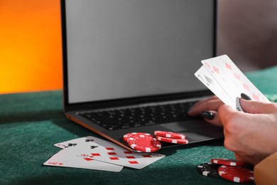 Photo of Online poker. Woman holding playing cards and using laptop at green table, closeup