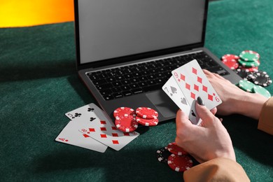 Photo of Online poker. Woman holding playing cards and using laptop at green table, closeup