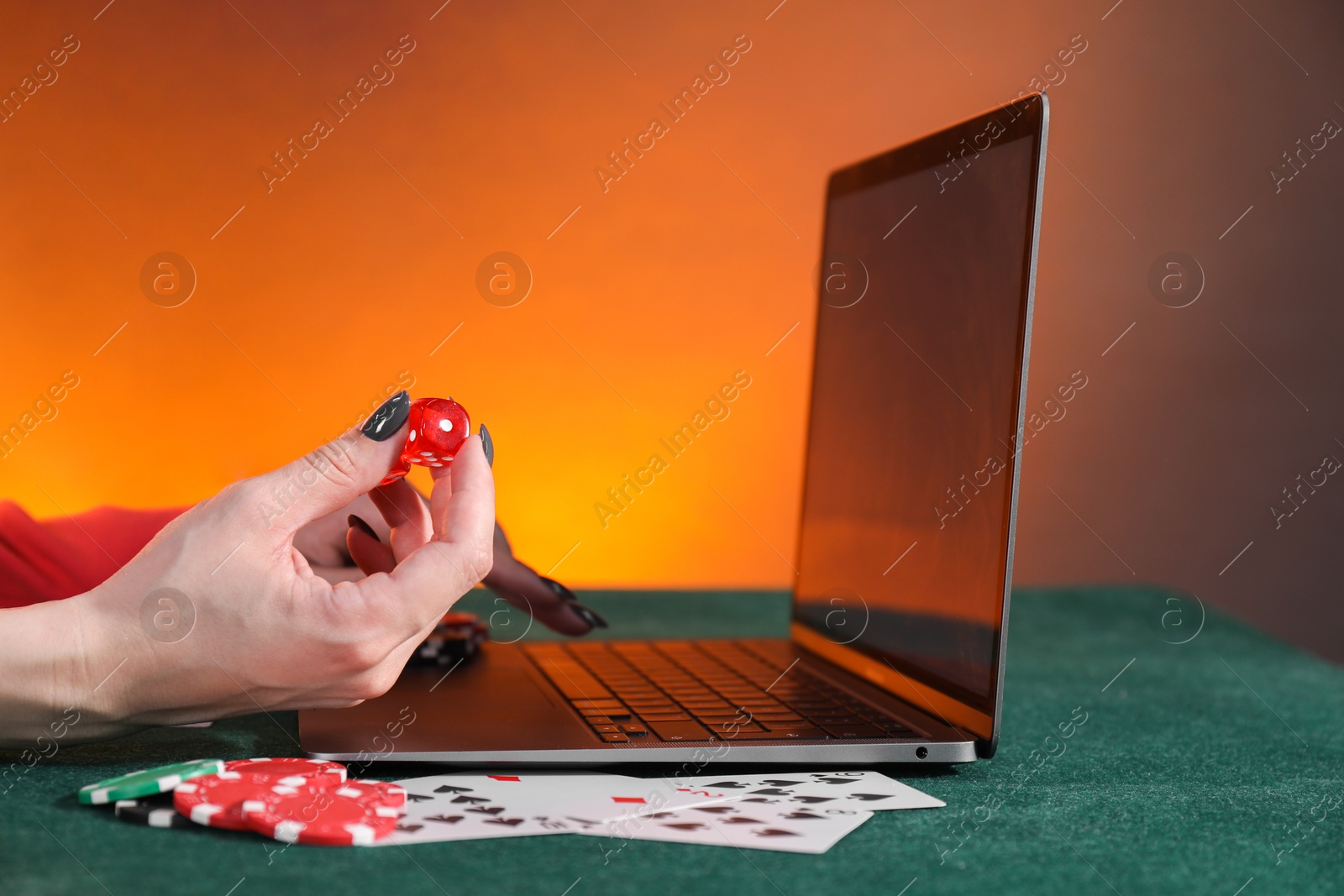 Photo of Online poker. Woman holding dice and using laptop at green table, closeup