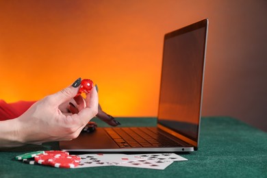 Photo of Online poker. Woman holding dice and using laptop at green table, closeup