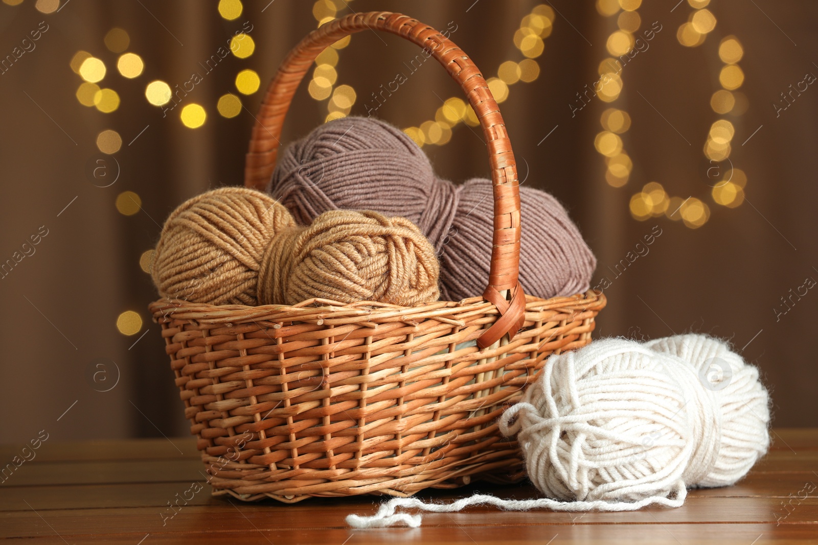 Photo of Knitting material. Wicker basket with skeins of soft yarn on wooden table