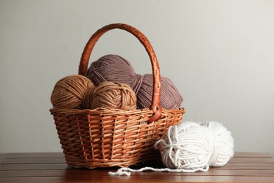 Photo of Knitting material. Wicker basket with skeins of soft yarn on wooden table