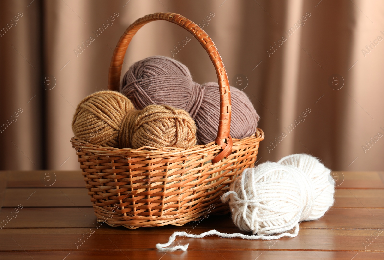 Photo of Knitting material. Wicker basket with skeins of soft yarn on wooden table