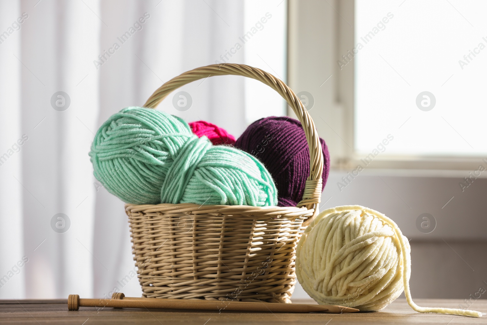 Photo of Skeins of soft yarn and knitting needles on wooden table indoors