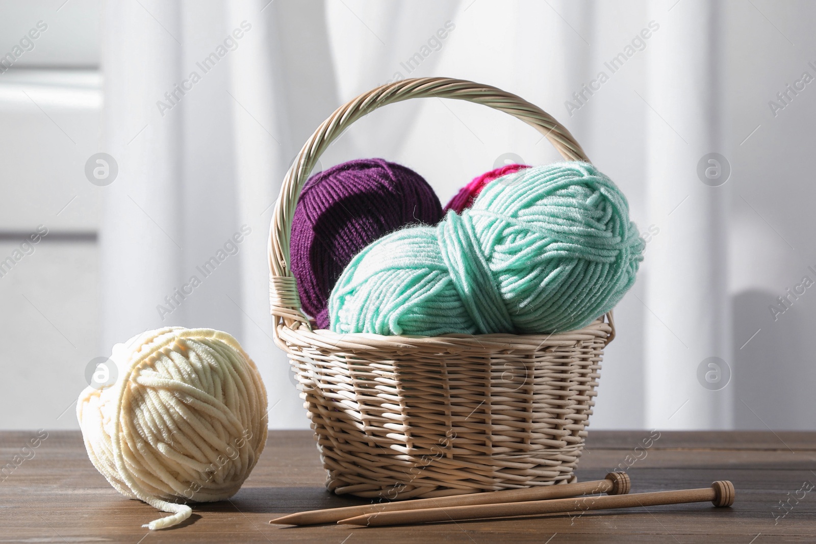 Photo of Skeins of soft yarn and knitting needles on wooden table indoors