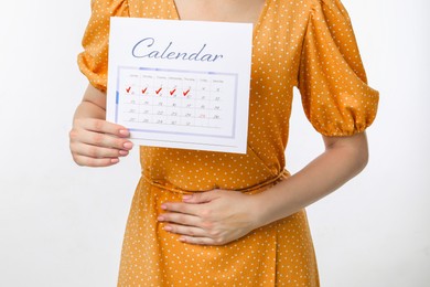 Woman holding calendar with marked menstrual cycle days and suffering from abdominal pain on white background, closeup