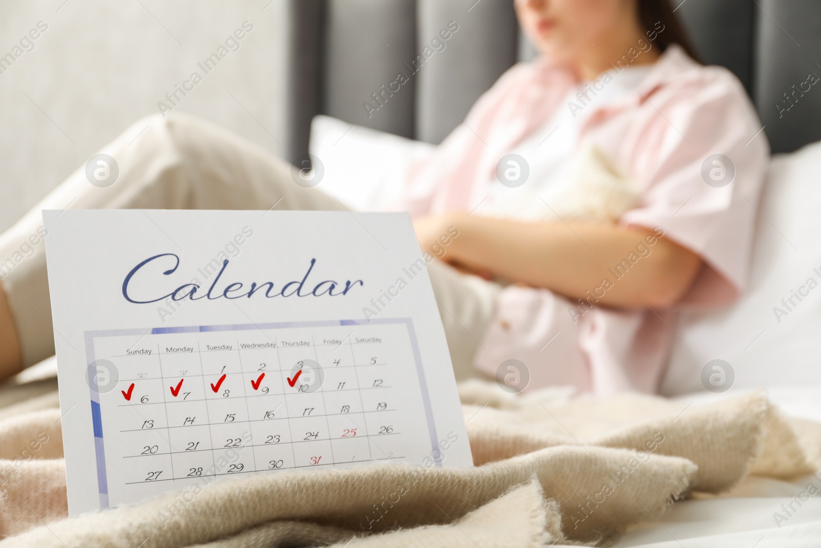 Photo of Woman suffering from abdominal pain in bed at home, focus on calendar with marked menstrual cycle days