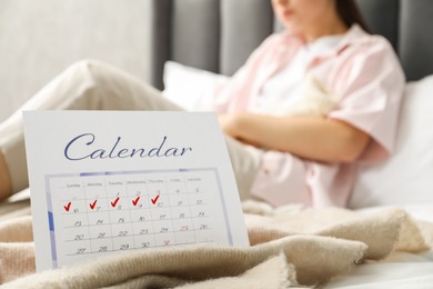 Woman suffering from abdominal pain in bed at home, focus on calendar with marked menstrual cycle days