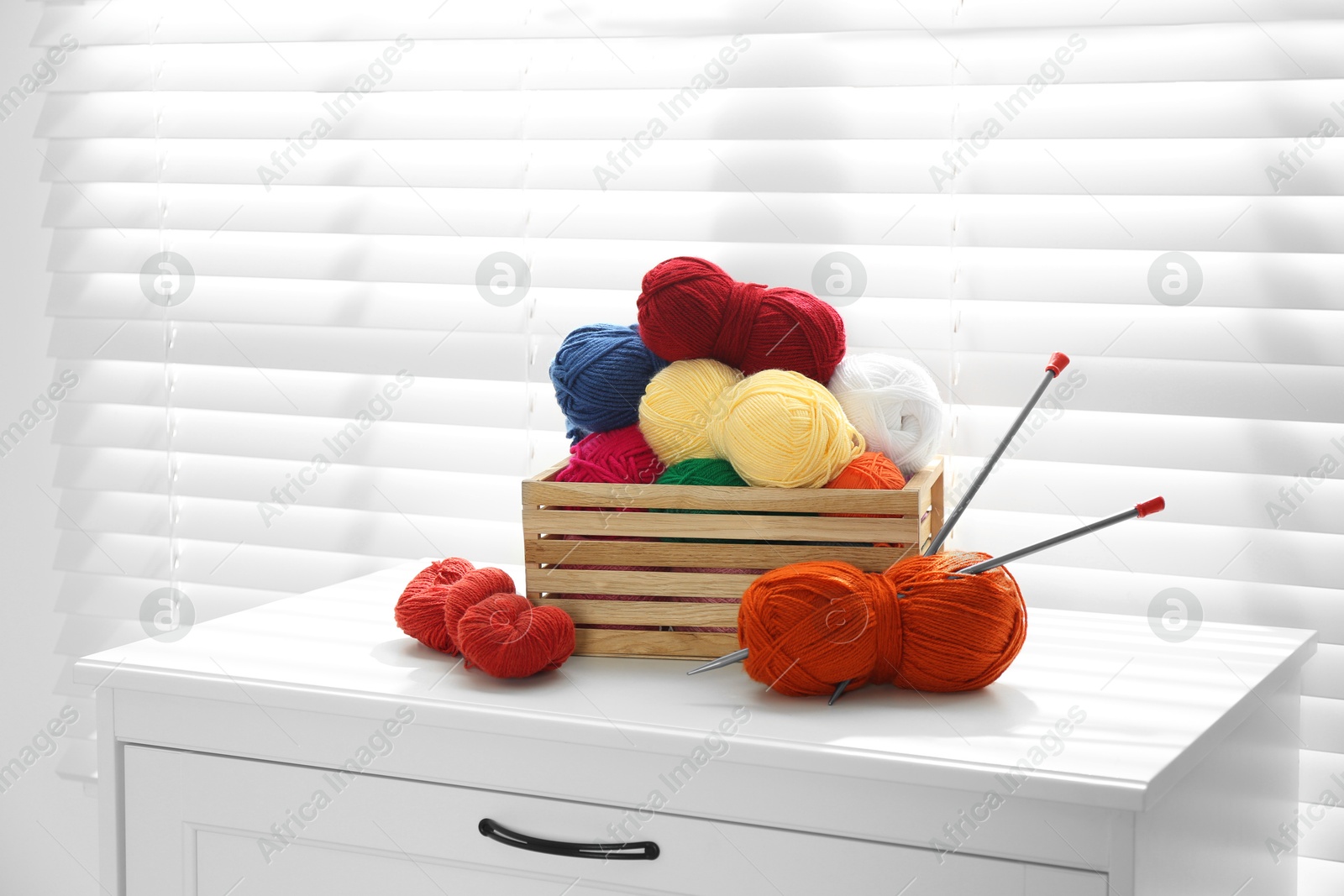 Photo of Soft yarn in crate and knitting needles on chest of drawers indoors