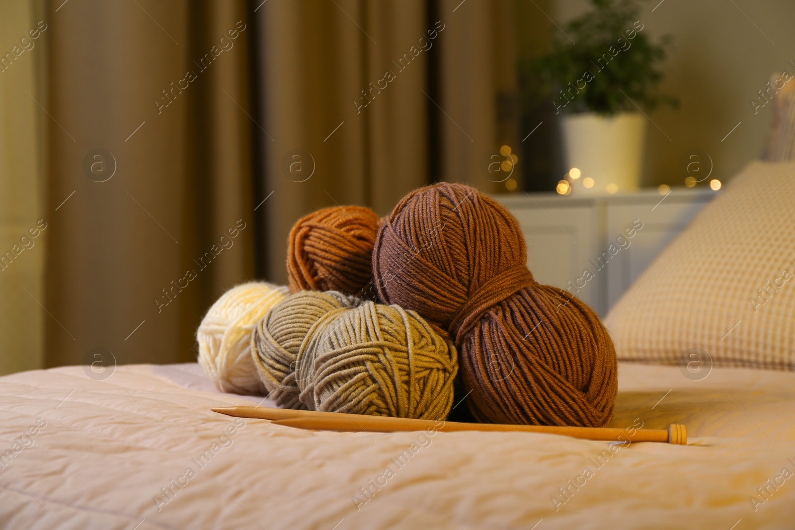 Photo of Skeins of soft yarn and knitting needles on bed indoors