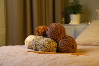 Photo of Skeins of soft yarn and knitting needles on bed indoors