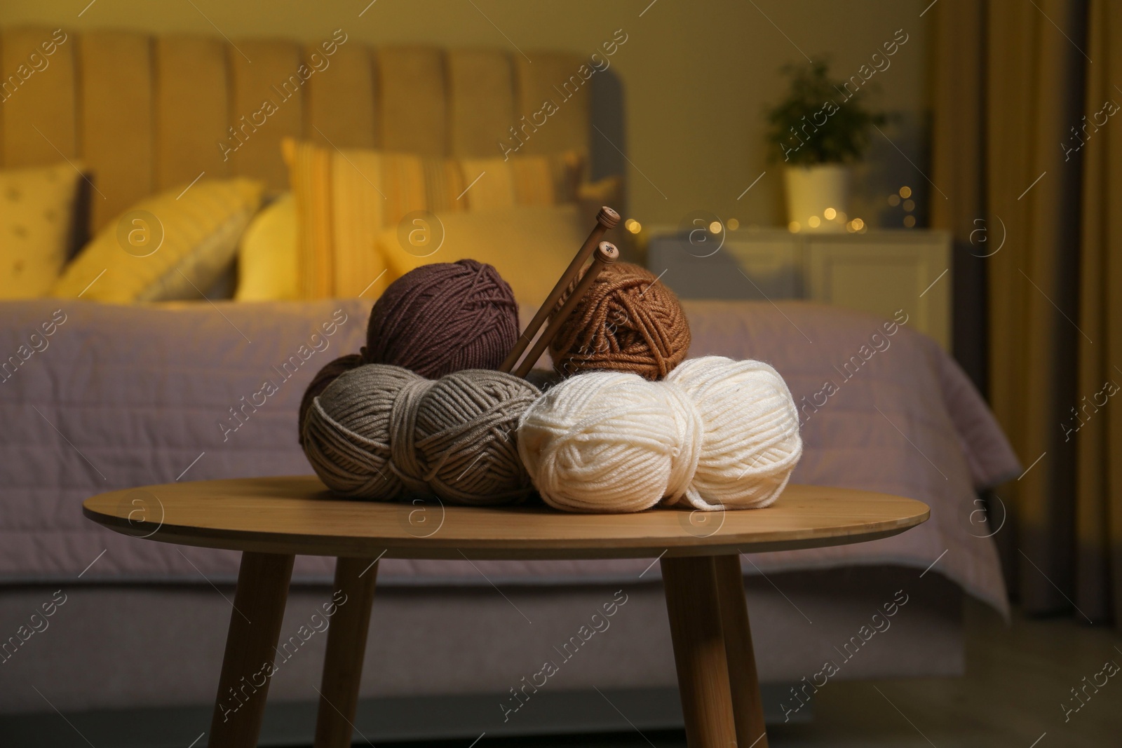 Photo of Skeins of soft yarn and knitting needles on wooden table indoors