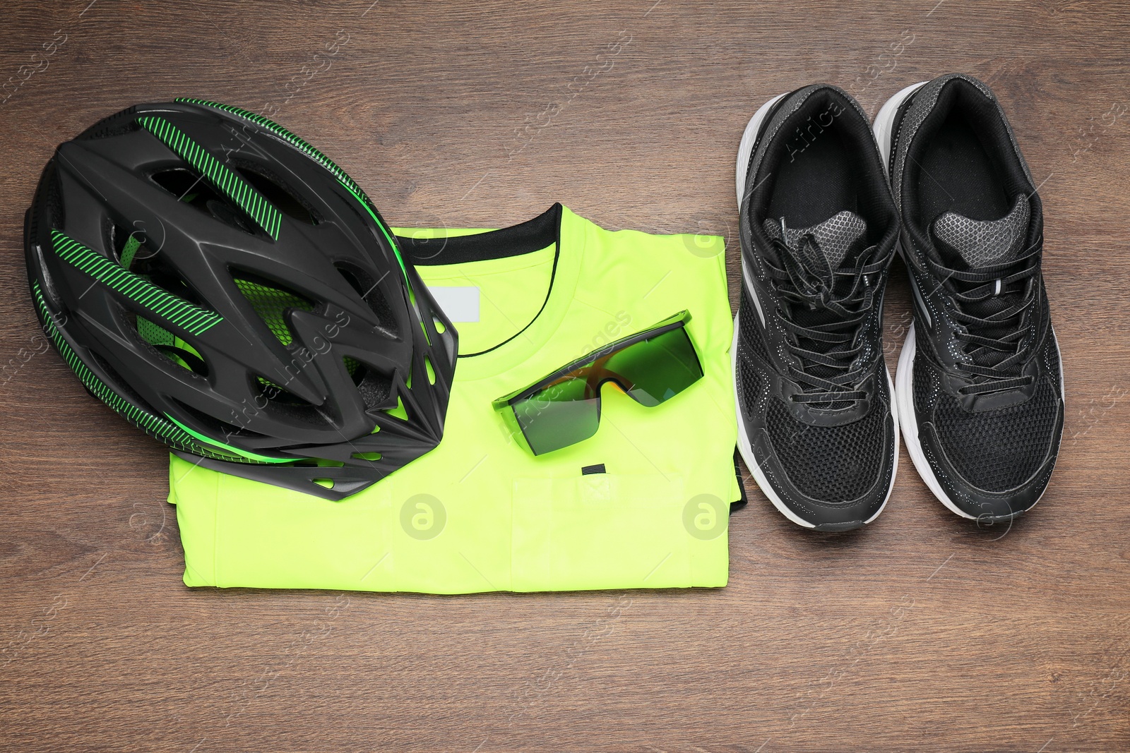 Photo of Bicycle helmet, sneakers, goggles and shirt on wooden background, flat lay