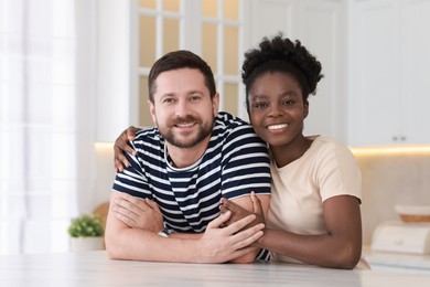 International relationships. Portrait of lovely couple at white marble table in kitchen