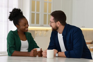 International relationships. Lovely couple enjoying hot drinks at white marble table in kitchen