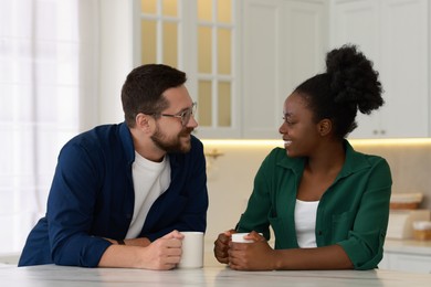 Photo of International relationships. Lovely couple enjoying hot drinks at white marble table in kitchen