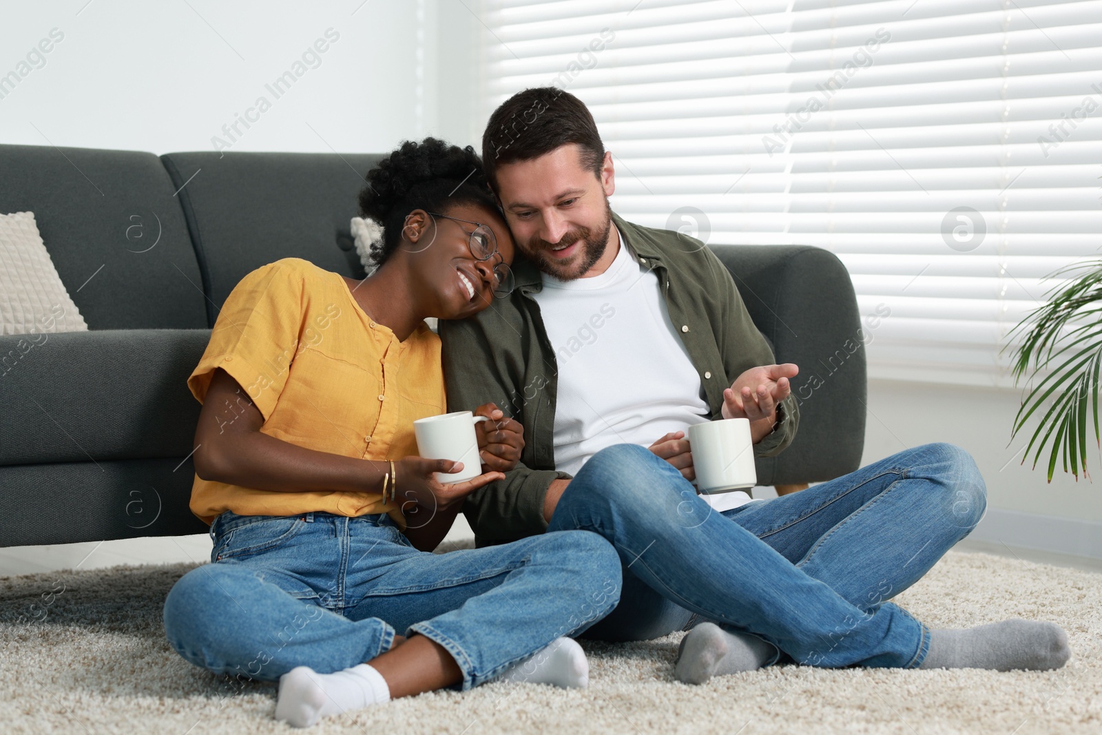 Photo of International relationships. Lovely couple enjoying hot drinks on floor at home