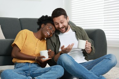 Photo of International relationships. Lovely couple enjoying hot drinks on floor at home