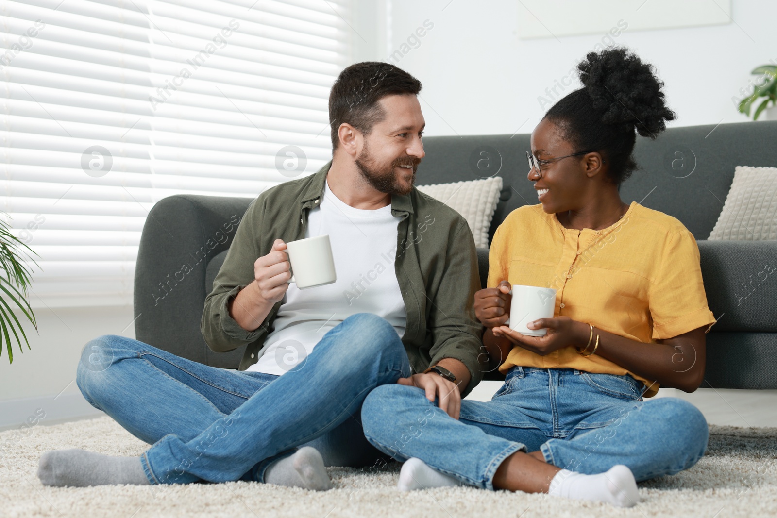 Photo of International relationships. Lovely couple enjoying hot drinks on floor at home