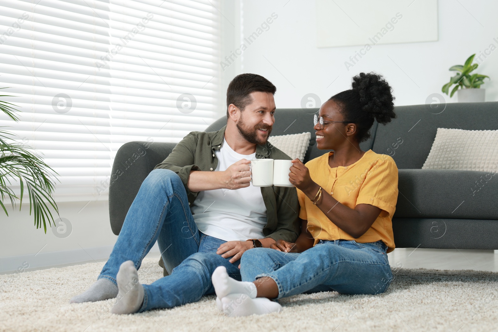 Photo of International relationships. Lovely couple enjoying hot drinks on floor at home