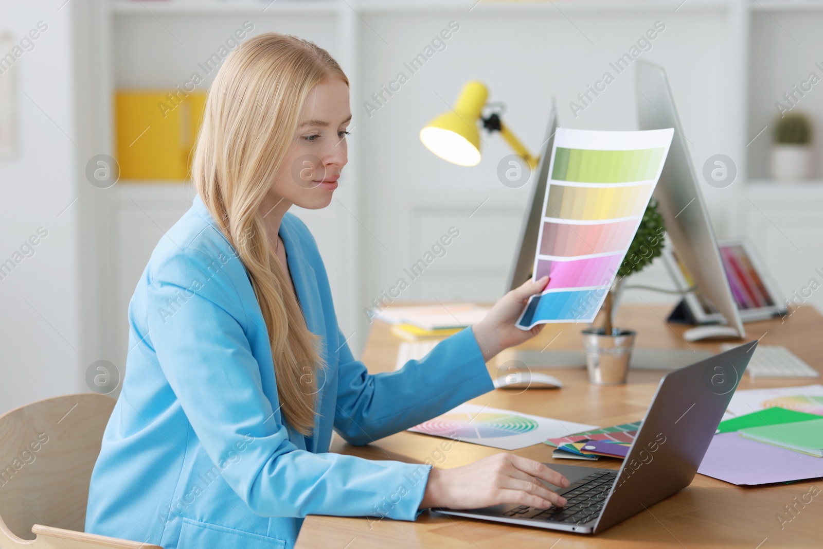 Photo of Designer working with laptop and color palette at table in office