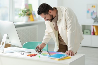 Photo of Designer with color samples working at table in office