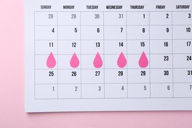 Photo of Menstruation. Calendar with marked dates on pink background, top view