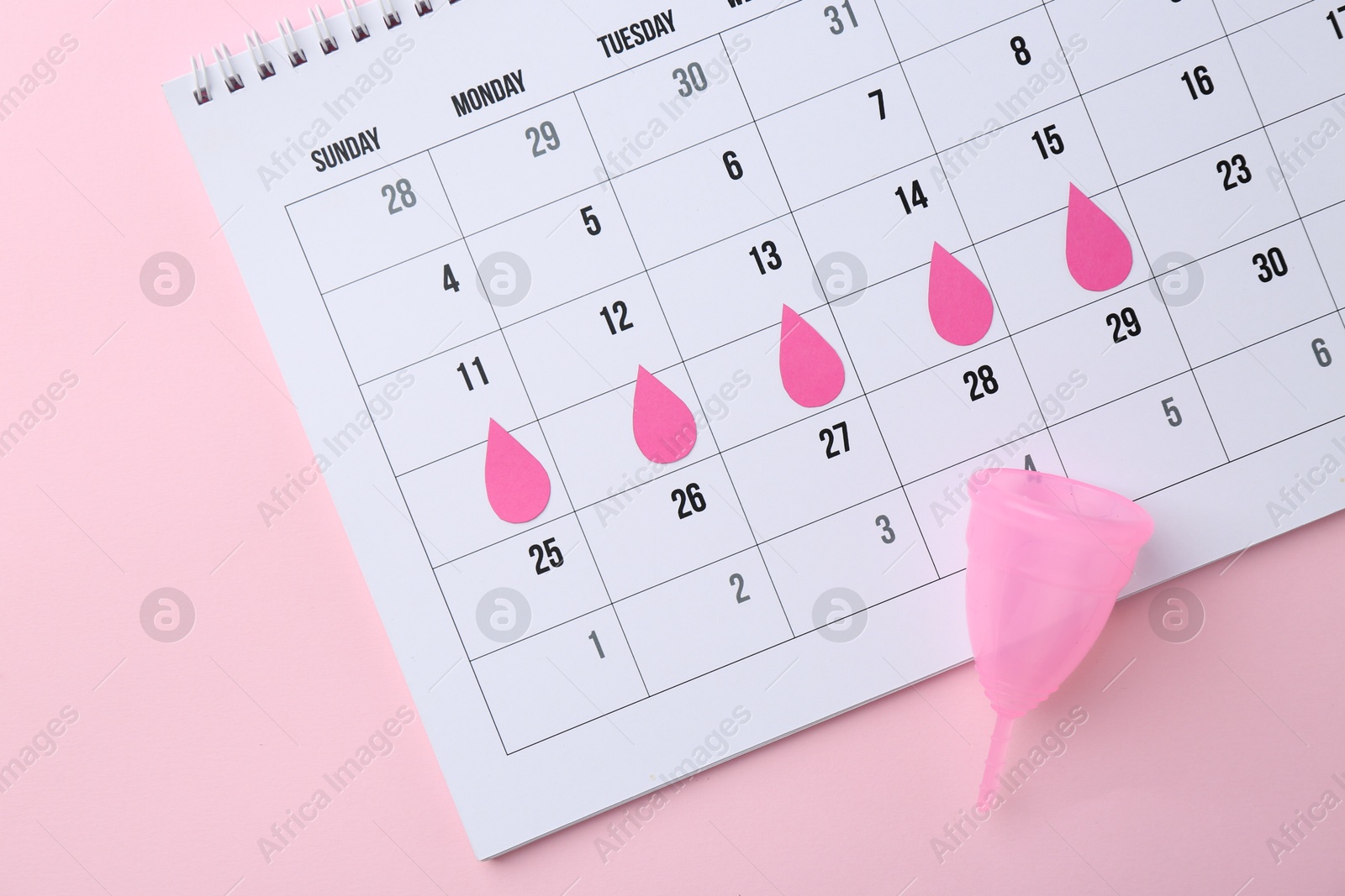 Photo of Calendar with marked dates and menstrual cup on pink background, top view