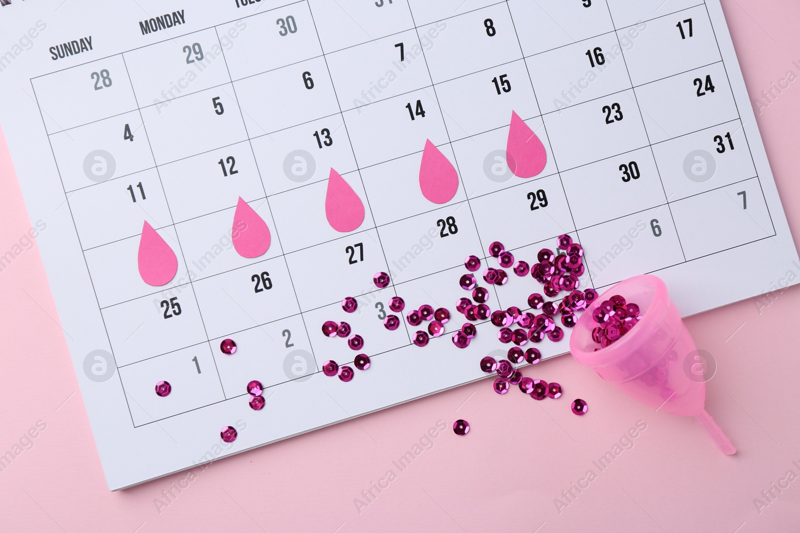 Photo of Calendar with marked dates and menstrual cup on pink background, top view