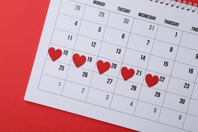 Photo of Menstruation. Calendar with marked dates on red background, top view