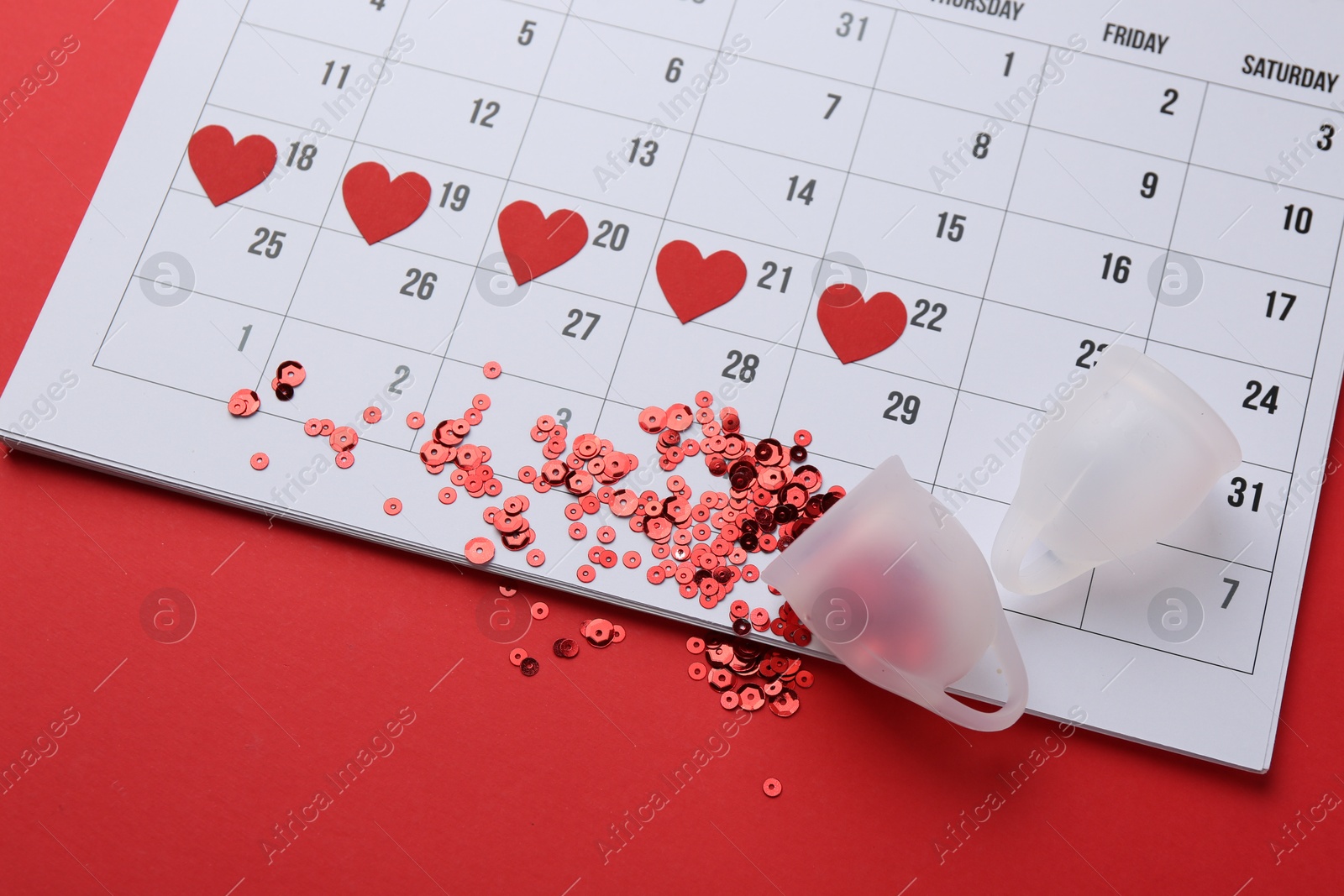 Photo of Calendar with marked dates and menstrual cups on red background