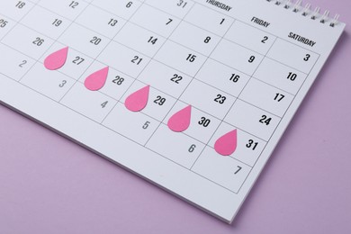 Menstruation. Calendar with marked dates on violet background, closeup