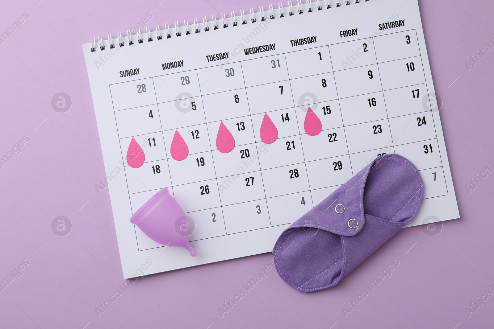 Photo of Calendar with marked dates, reusable pad and menstrual cup on violet background, top view