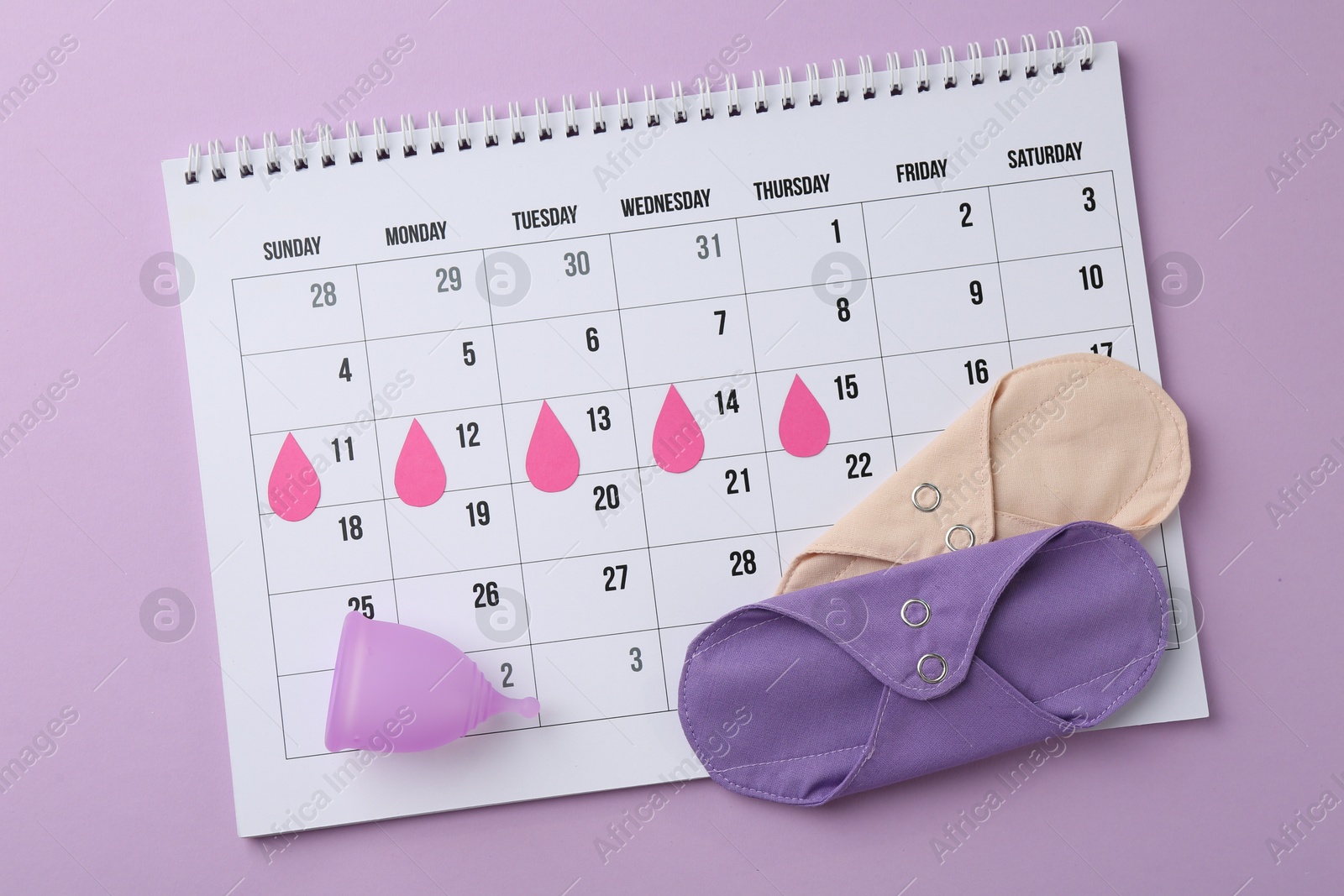 Photo of Calendar with marked dates, reusable pads and menstrual cup on violet background, top view