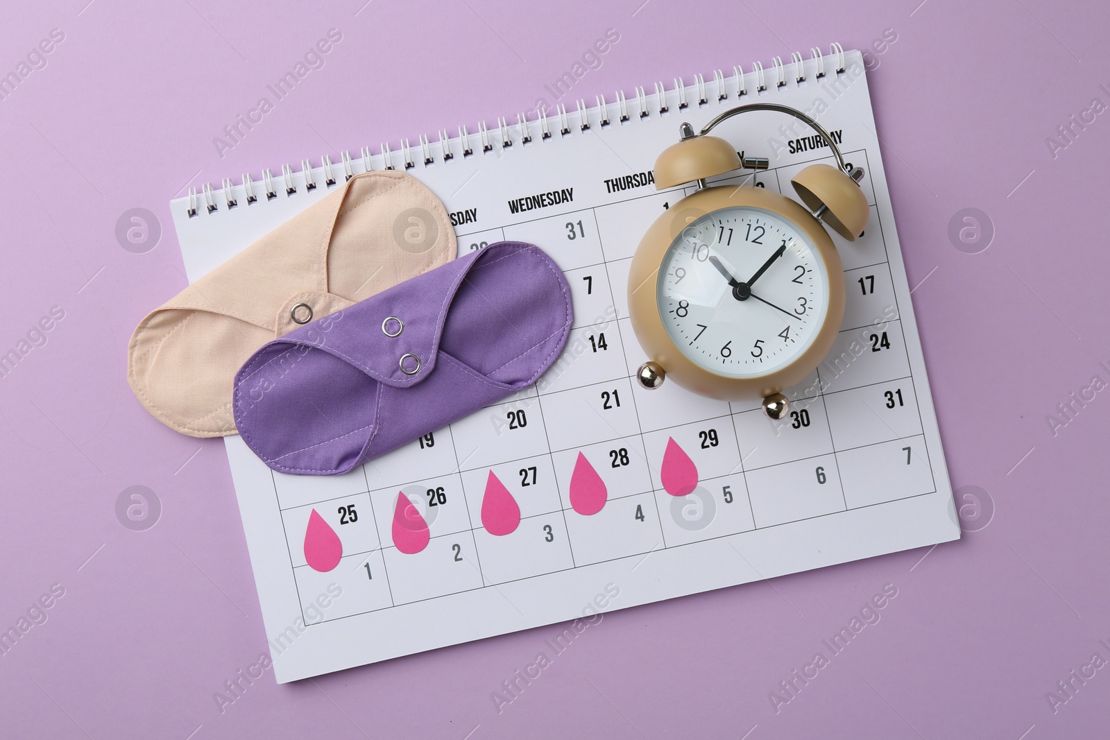 Photo of Calendar with marked dates, reusable pads and alarm clock on violet background, top view