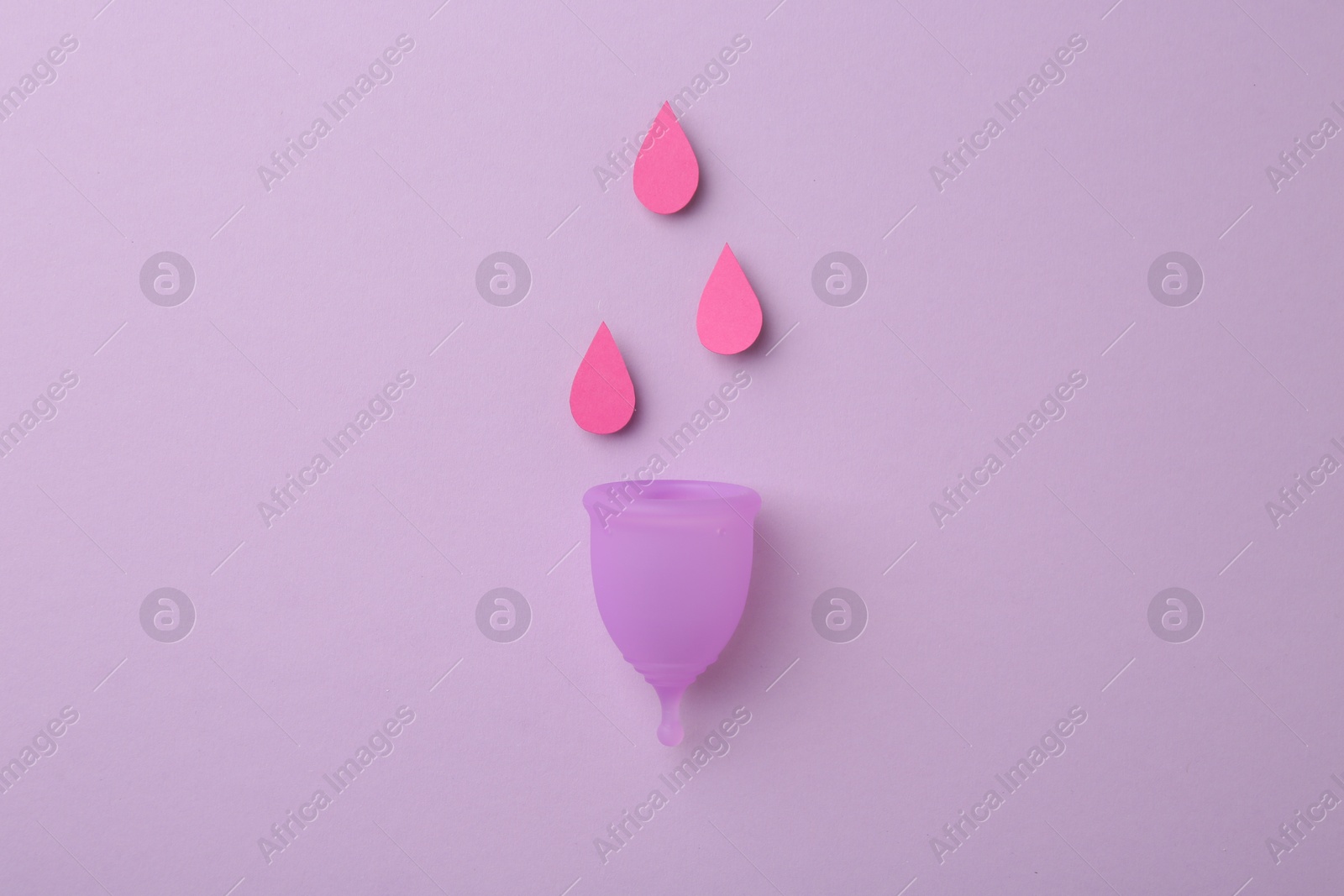 Photo of Menstrual cup with drops on violet background, top view