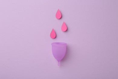 Photo of Menstrual cup with drops on violet background, top view